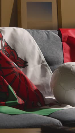 Vertical-Video-Of-Sofa-In-Lounge-With-Iranian-And-Welsh-Flags-And-Ball-As-Fans-Prepare-To-Watch-Football-Soccer-Match-On-TV